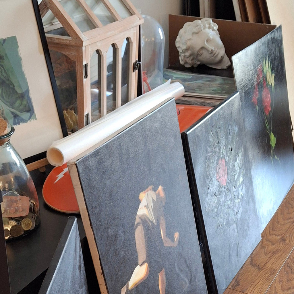Artistic display with paintings, a lantern, and books on a wooden surface.